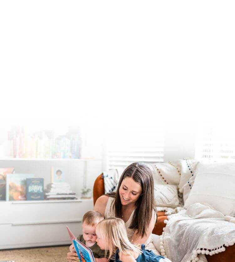 Mother reads with two small children on the floor of living room.