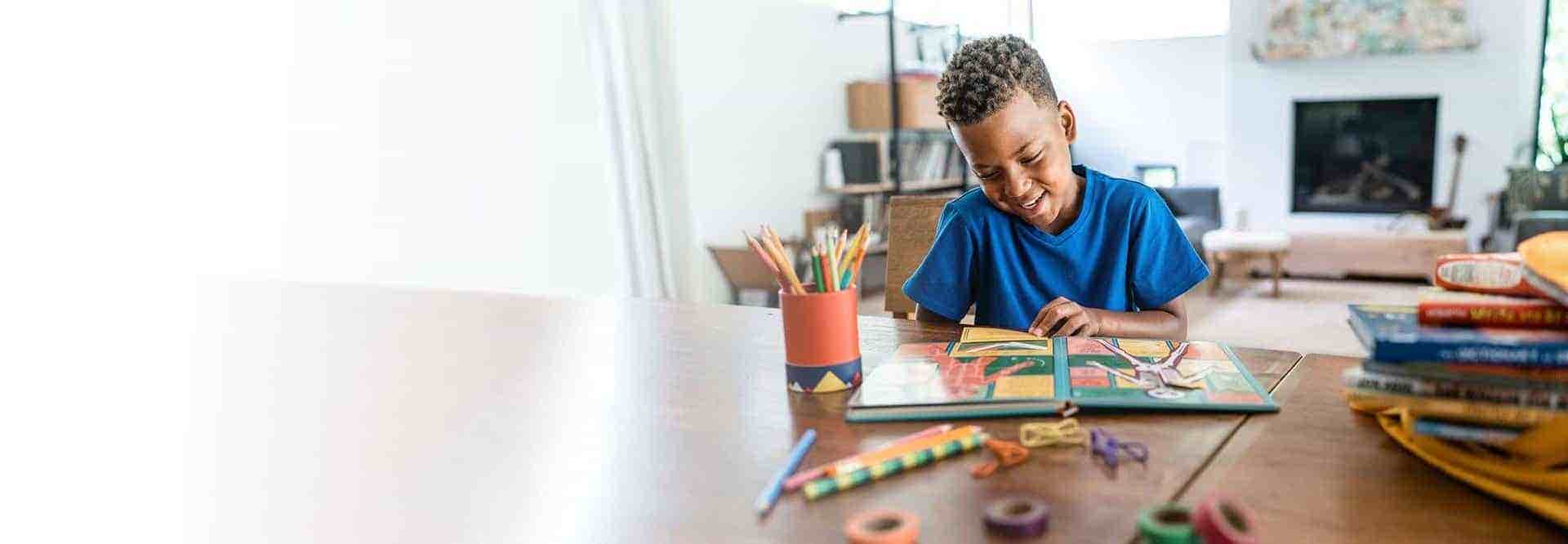 Young boy reads a book at the kitchen table.