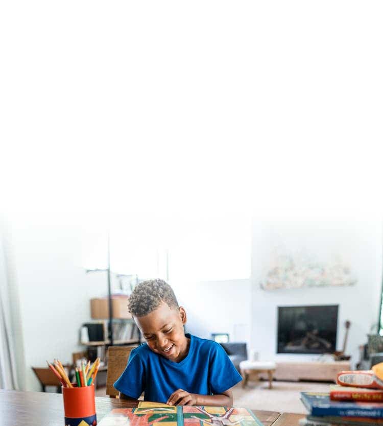 Young boy reads a book at the kitchen table.