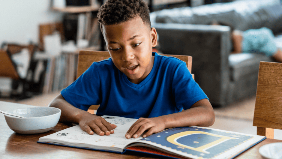 Young boy reads a book at the kitchen table