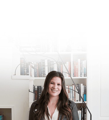 Jess Ewing, Literati's Founder, stands in front of a large bookcase.