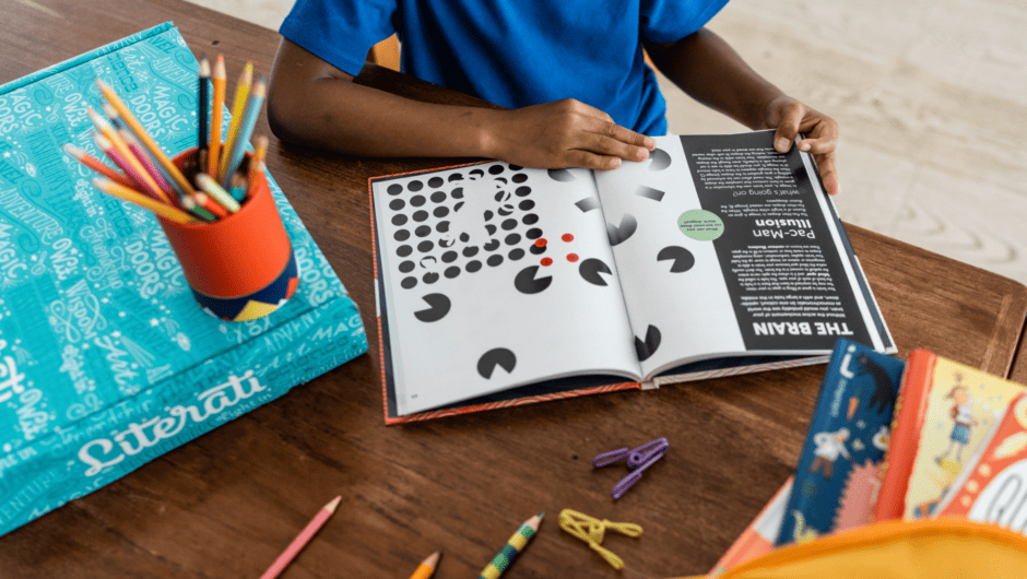Overhead shot of young boy working on activity book with Literati Box nearby