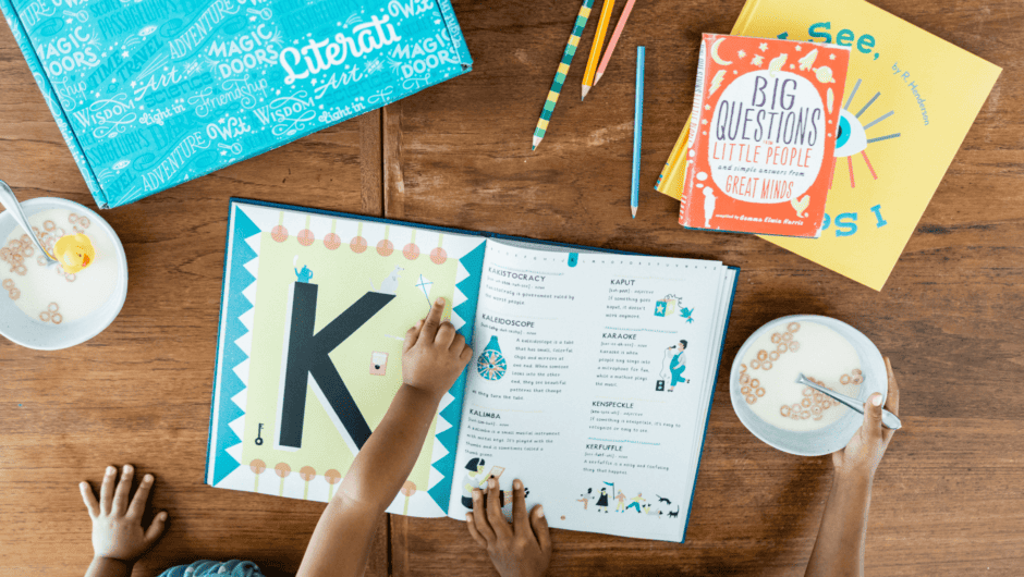 A child points to something on the page of an open book with cereal bowls, two more books, and a Literati box nearby.